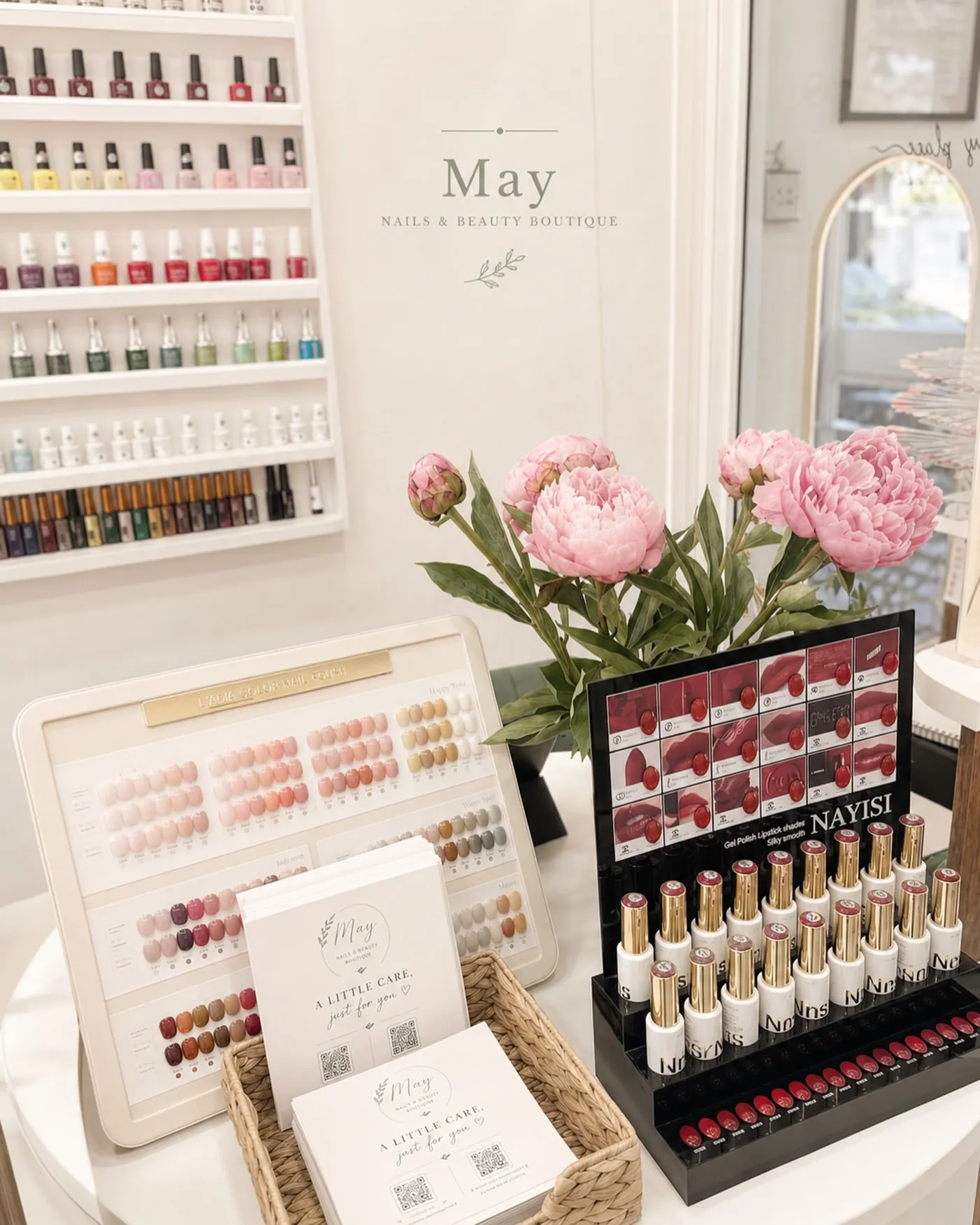 The polish display: shelves of bottles, a tester stand and pink peonies